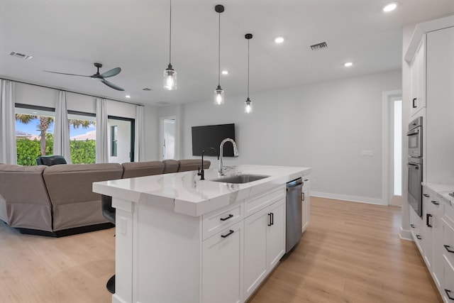 kitchen with sink, light stone countertops, an island with sink, white cabinets, and appliances with stainless steel finishes