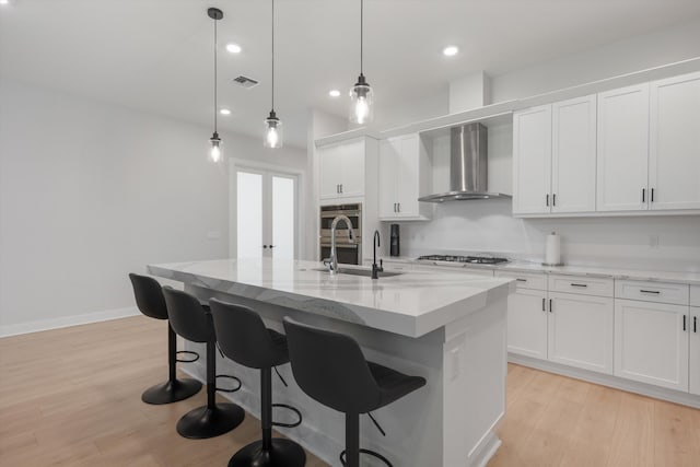 kitchen featuring pendant lighting, an island with sink, light hardwood / wood-style floors, and white cabinetry