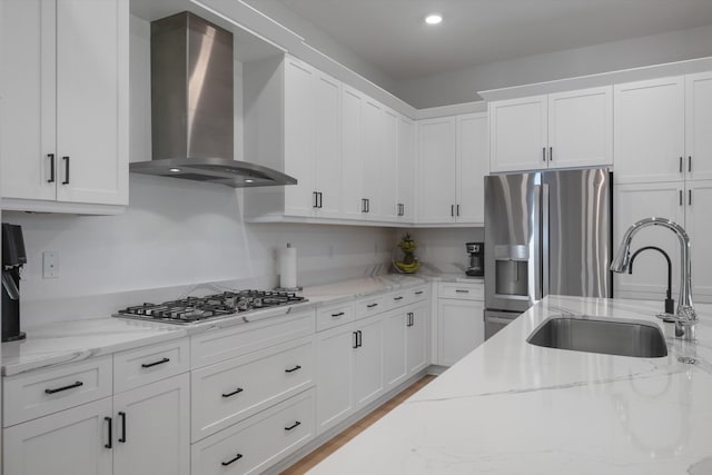 kitchen with light stone countertops, stainless steel appliances, white cabinets, wall chimney exhaust hood, and sink