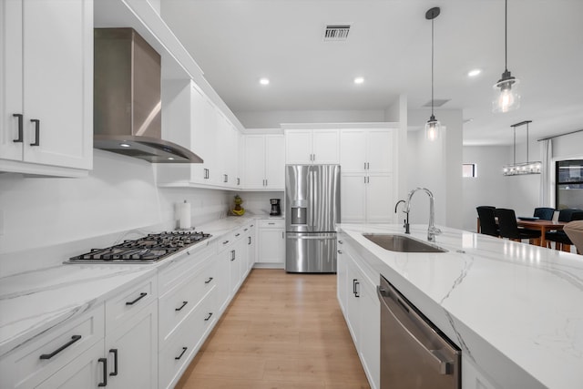 kitchen with wall chimney exhaust hood, light wood-type flooring, sink, stainless steel appliances, and white cabinetry