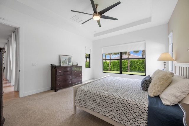 bedroom featuring ceiling fan, a raised ceiling, and light carpet