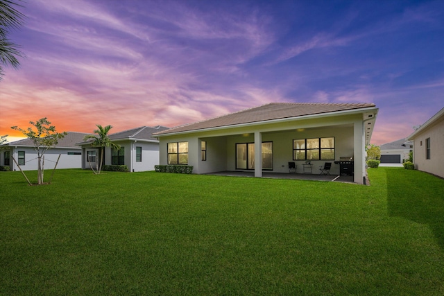 back house at dusk with a lawn and a patio area