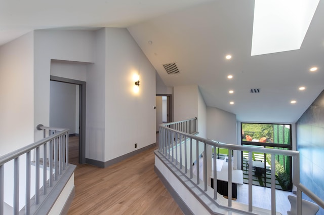 hall with a skylight, light hardwood / wood-style floors, and high vaulted ceiling