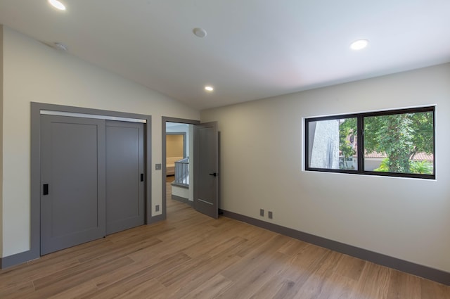 unfurnished bedroom with light wood-type flooring, lofted ceiling, and a closet