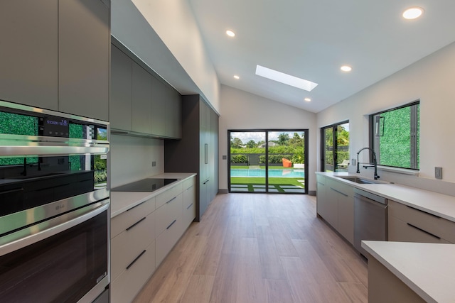 kitchen featuring light hardwood / wood-style floors, gray cabinets, stainless steel appliances, lofted ceiling with skylight, and sink