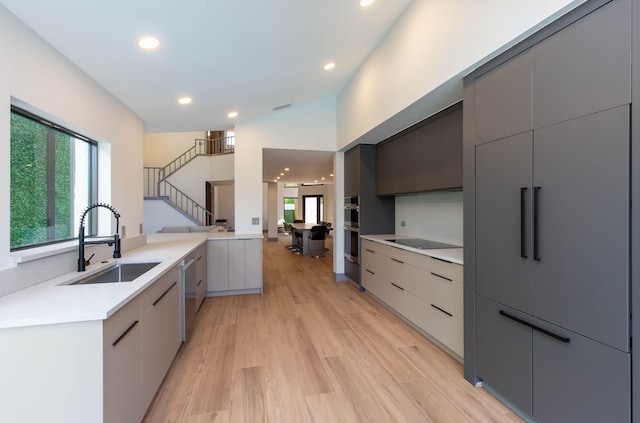 kitchen with sink, vaulted ceiling, gray cabinets, stainless steel appliances, and light hardwood / wood-style floors