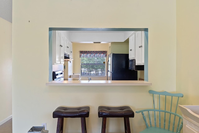 kitchen featuring kitchen peninsula, black fridge, a breakfast bar, white cabinetry, and electric stove