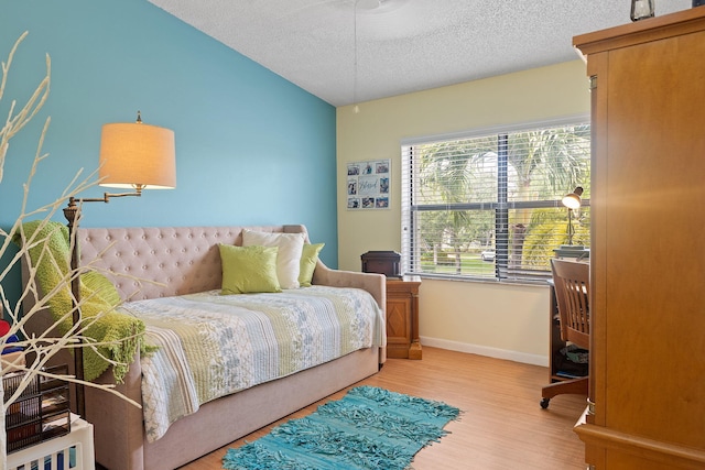 bedroom featuring a textured ceiling, light wood-type flooring, and vaulted ceiling