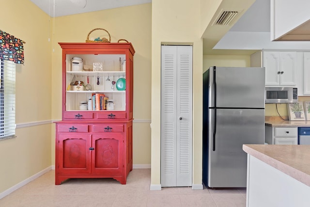 kitchen with vaulted ceiling, appliances with stainless steel finishes, white cabinets, and light tile patterned floors