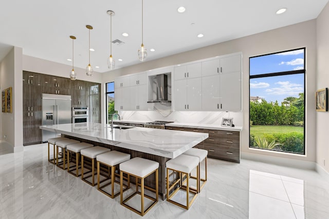 kitchen featuring wall chimney exhaust hood, dark brown cabinetry, stainless steel appliances, and a center island with sink