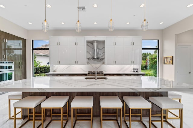 kitchen with a large island with sink, a healthy amount of sunlight, pendant lighting, and ventilation hood