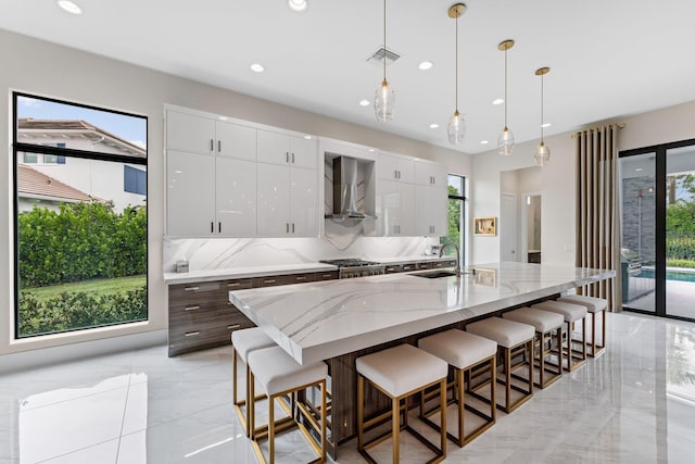 kitchen featuring a healthy amount of sunlight, wall chimney range hood, and white cabinets