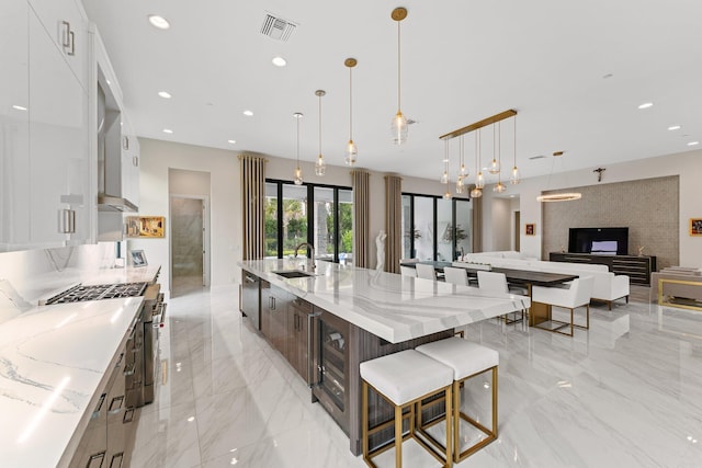 kitchen with light stone countertops, sink, a large island, decorative light fixtures, and white cabinets