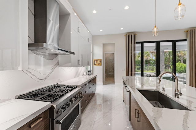 kitchen with wall chimney range hood, white cabinets, high end stove, pendant lighting, and sink