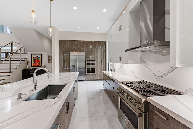 kitchen with wall chimney range hood, high quality appliances, sink, pendant lighting, and white cabinetry