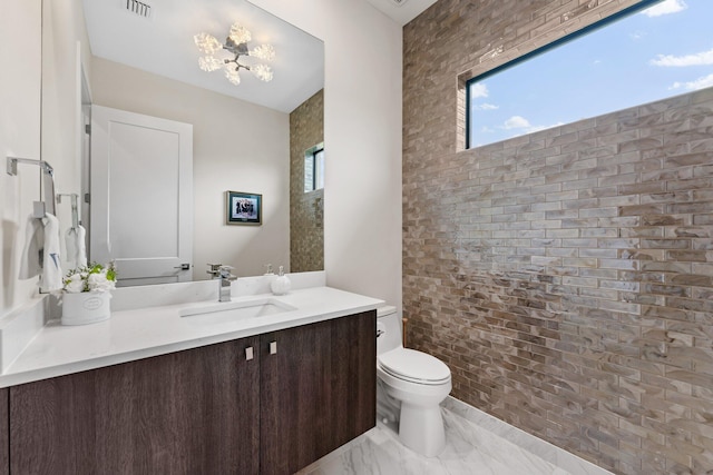 bathroom featuring vanity, toilet, and brick wall