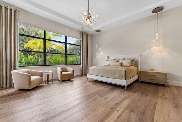 bedroom with a chandelier, light hardwood / wood-style flooring, and a raised ceiling