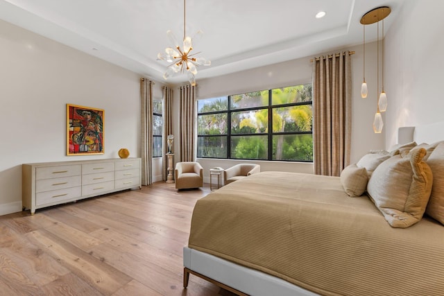 bedroom with light hardwood / wood-style floors, a notable chandelier, and a raised ceiling