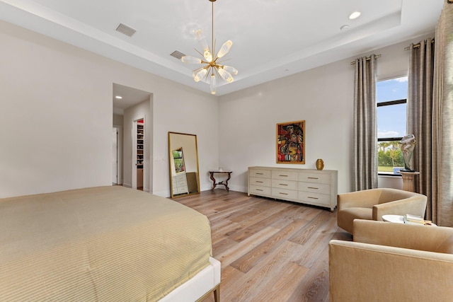 bedroom with light hardwood / wood-style floors, a notable chandelier, and a tray ceiling