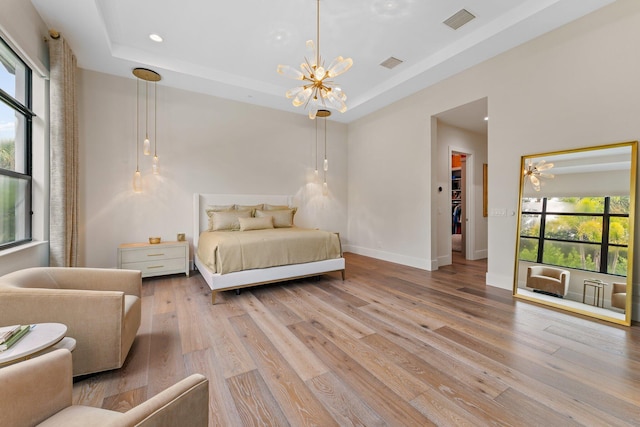 bedroom featuring a tray ceiling, a chandelier, multiple windows, and light wood-type flooring