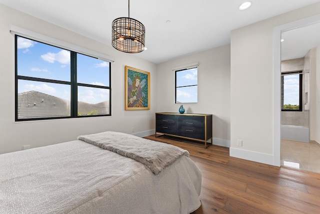 bedroom with ensuite bath, a notable chandelier, and dark hardwood / wood-style flooring