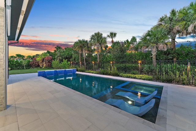 pool at dusk with an in ground hot tub and a patio area