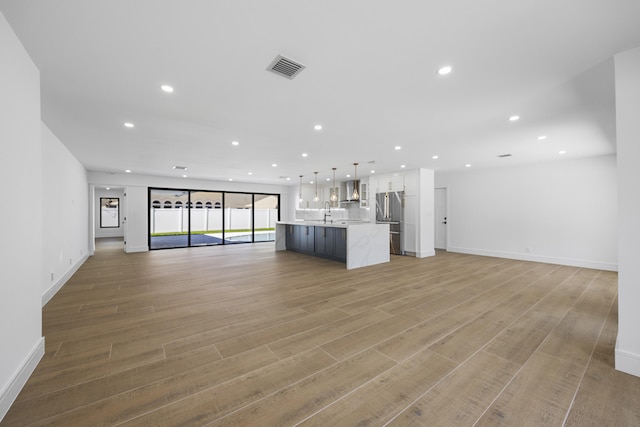 unfurnished living room featuring a sink, light wood finished floors, baseboards, visible vents, and recessed lighting