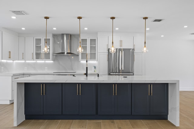kitchen featuring visible vents, freestanding refrigerator, light stone countertops, wall chimney exhaust hood, and white cabinetry