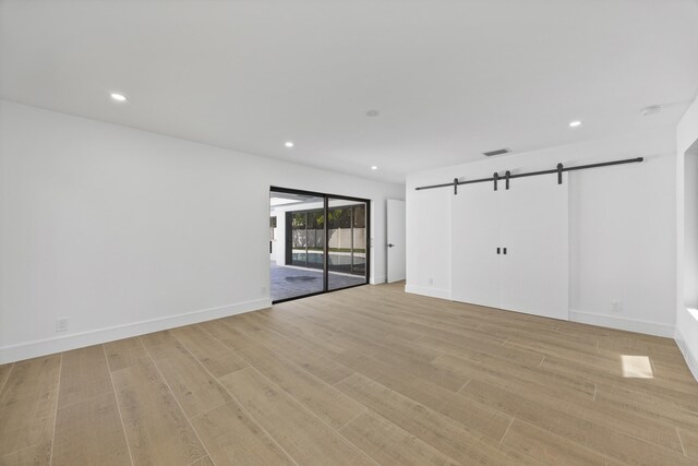 spare room with a barn door, light wood-type flooring, baseboards, and recessed lighting
