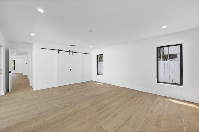 empty room with recessed lighting, a barn door, a wealth of natural light, and light wood-style flooring