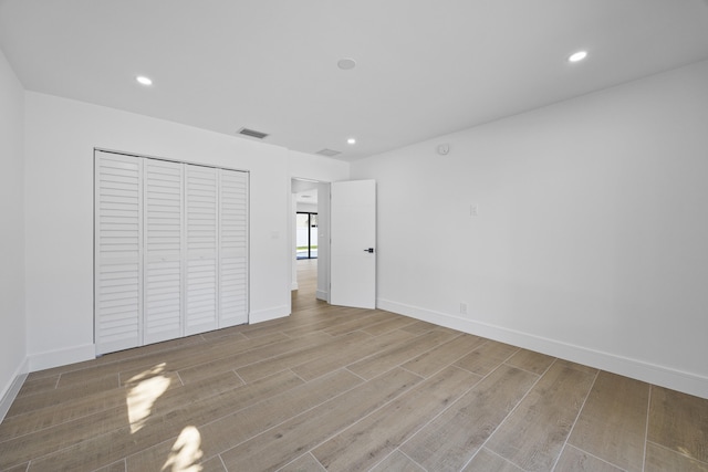 unfurnished bedroom with baseboards, visible vents, recessed lighting, wood finished floors, and a closet