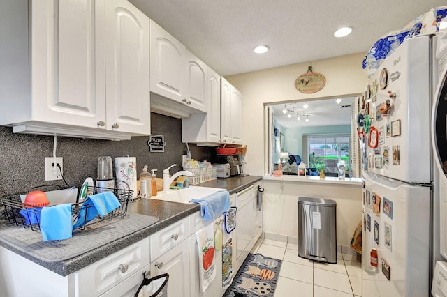 kitchen with dark countertops, decorative backsplash, light tile patterned flooring, white cabinets, and white appliances