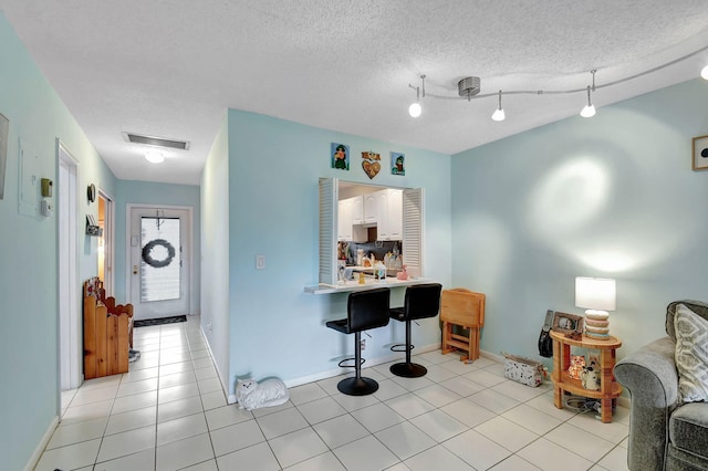 interior space with light tile patterned floors, a kitchen bar, visible vents, a textured ceiling, and baseboards