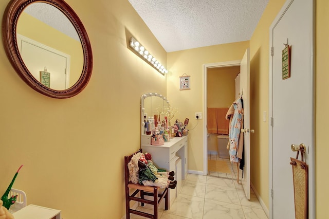 corridor with marble finish floor, a textured ceiling, and baseboards