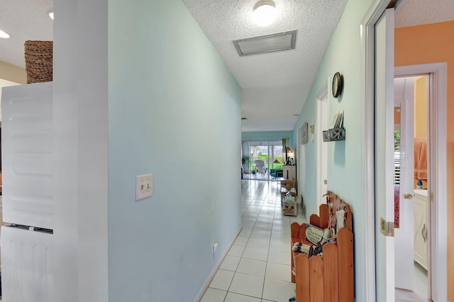 hall featuring light tile patterned floors, baseboards, visible vents, and a textured ceiling