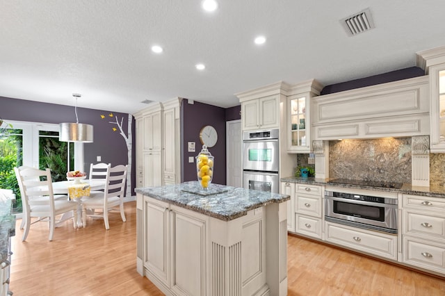 kitchen featuring light stone countertops, decorative light fixtures, tasteful backsplash, black electric cooktop, and double oven