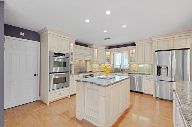 kitchen featuring sink, a center island, tasteful backsplash, light stone countertops, and appliances with stainless steel finishes