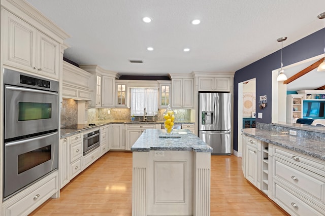 kitchen featuring appliances with stainless steel finishes, light stone counters, a kitchen island, decorative light fixtures, and backsplash