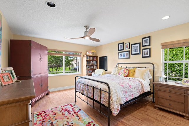 bedroom featuring a textured ceiling, ceiling fan, light hardwood / wood-style flooring, and multiple windows