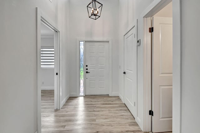 foyer entrance with light wood-type flooring, baseboards, and a notable chandelier