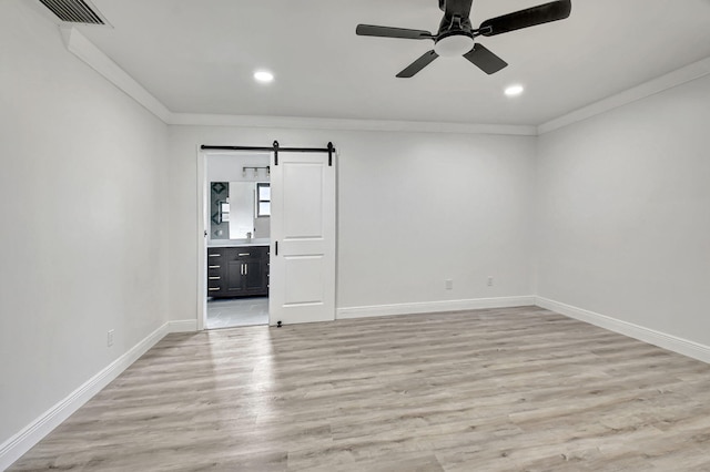 empty room featuring light wood-type flooring, a barn door, ceiling fan, and ornamental molding