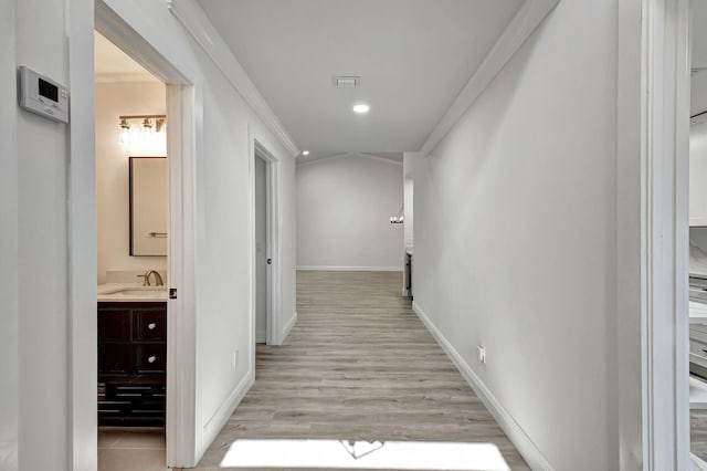 corridor with recessed lighting, a sink, light wood-style flooring, and baseboards