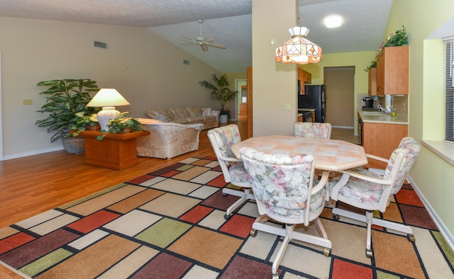 dining area featuring a textured ceiling, sink, vaulted ceiling, hardwood / wood-style floors, and ceiling fan