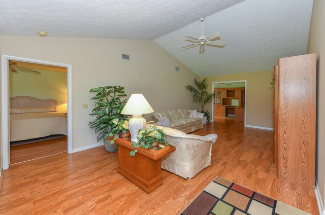 living room with light wood-type flooring, a textured ceiling, lofted ceiling, and ceiling fan