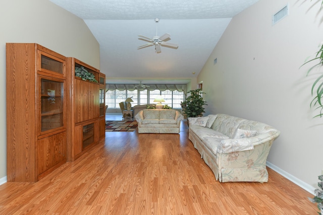 living room with light wood-type flooring, vaulted ceiling, ceiling fan, and a textured ceiling