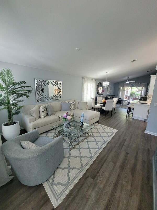 living room with ceiling fan with notable chandelier, dark wood-type flooring, and vaulted ceiling