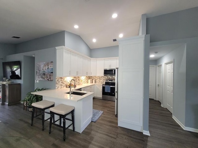 kitchen with sink, kitchen peninsula, a kitchen bar, appliances with stainless steel finishes, and dark hardwood / wood-style flooring