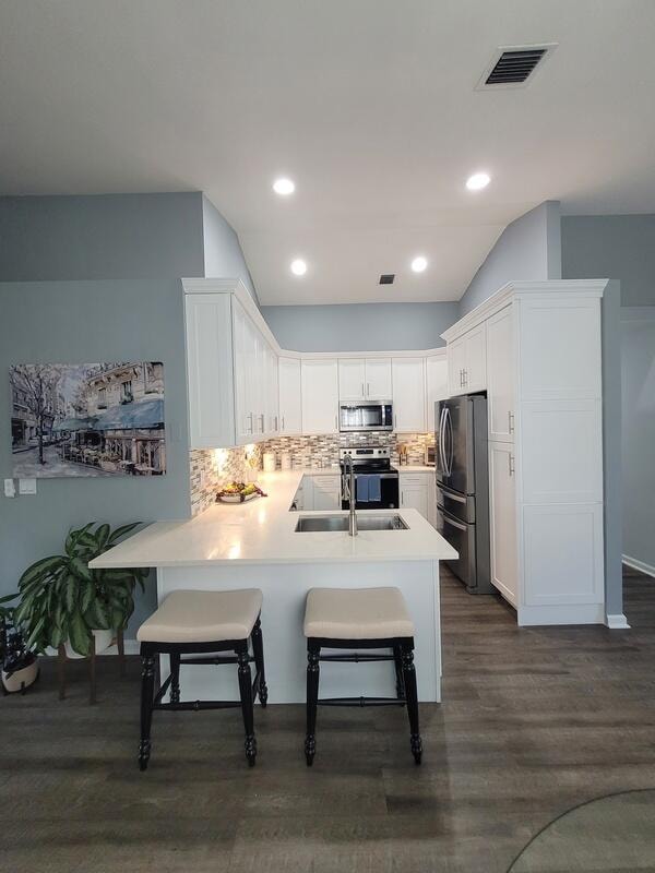 kitchen with appliances with stainless steel finishes, white cabinetry, kitchen peninsula, a breakfast bar area, and dark hardwood / wood-style flooring