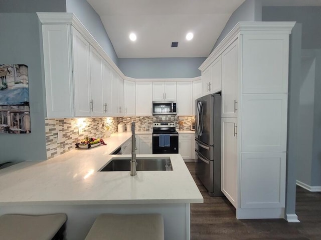 kitchen featuring kitchen peninsula, white cabinetry, a kitchen breakfast bar, appliances with stainless steel finishes, and dark hardwood / wood-style flooring