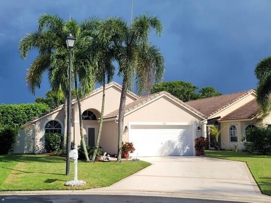 view of front facade with stucco siding, a tile roof, concrete driveway, a front yard, and a garage